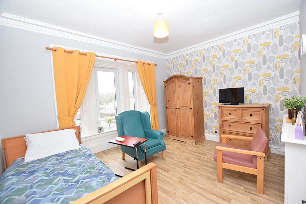 DSC_1840 Resident's bedroom with two chairs, wardrobe and a single bed.