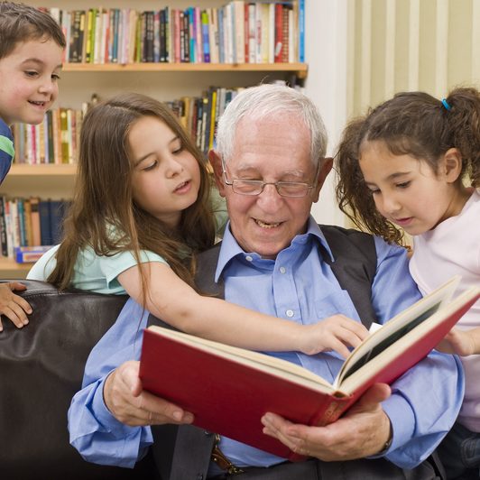 Elderly man reading a book with grandchildren on a visit