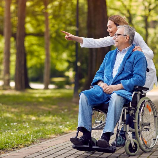 Nurse talking Elderly man in wheelchair for a walk outside