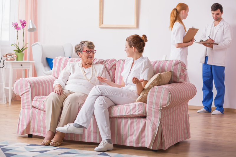 Care home staff sitting with elderly woman on a pink striped sofa